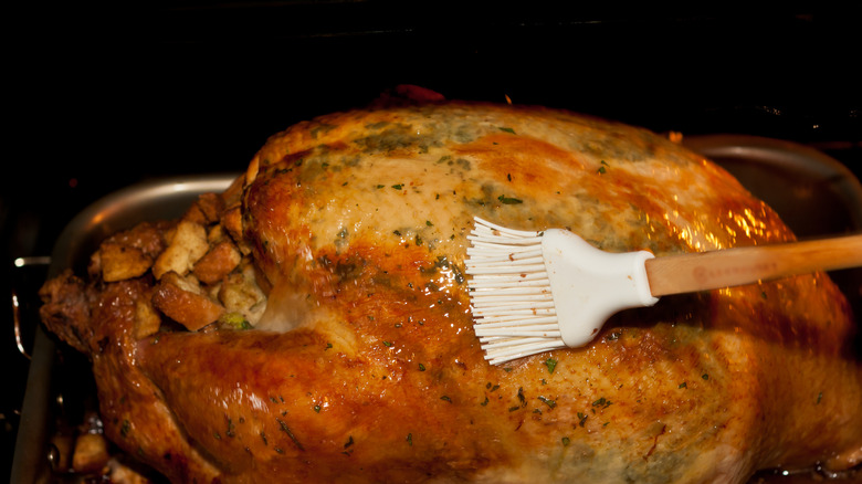 A white basting brush, brushing butter on a turkey