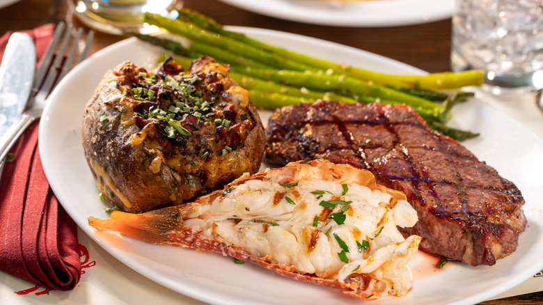 Steak served with lobster tail, stuffed potato, and asparagus