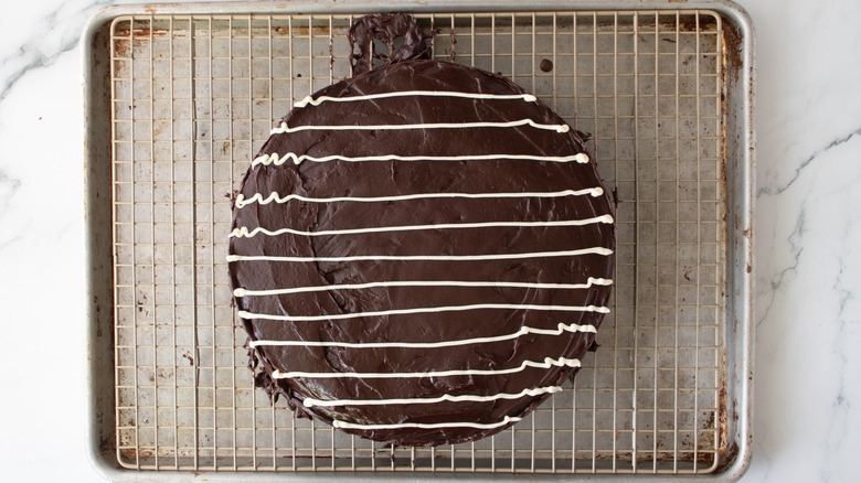 chocolate-frosted cake with a white drizzle on a metal rack