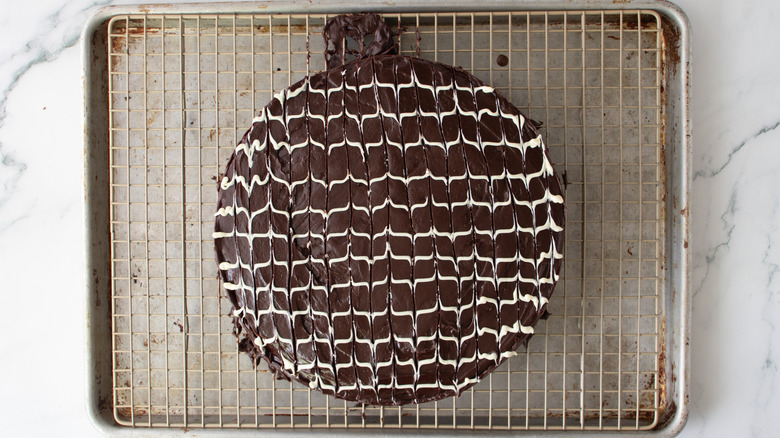 chocolate-frosted cake with a wavy white drizzle on a metal rack