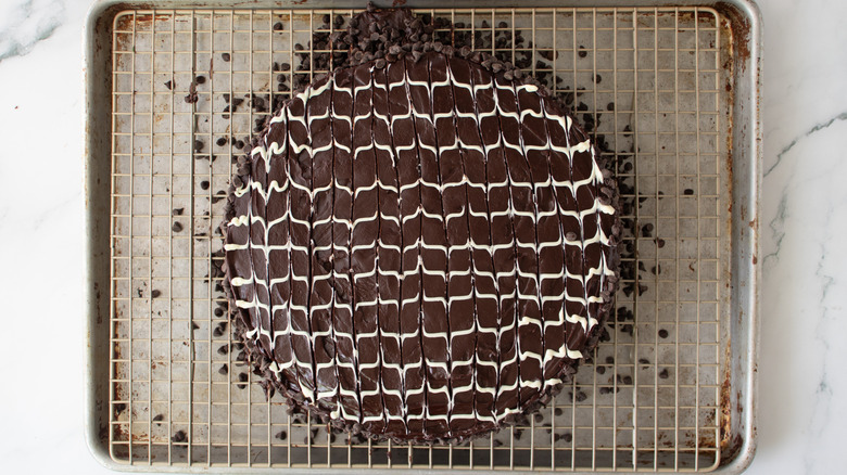 chocolate-frosted cake with a wavy white drizzle and mini chips on a metal rack