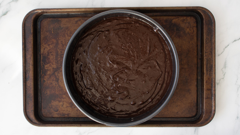 brownie batter in cake pan on larger baking sheet