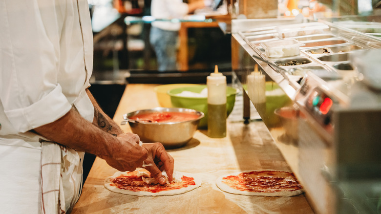 Chef prepares fresh pizzas at an assembly station