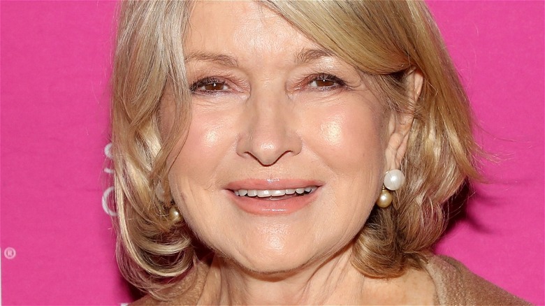 Martha Stewart wearing pearl earrings standing against a pink background