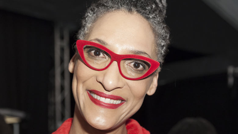 Carla Hall smiles with red glasses and red lipstick