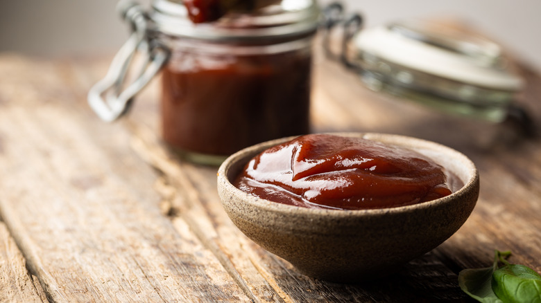 BBQ sauce in dish with more sauce in a glass jar, all on wooden table