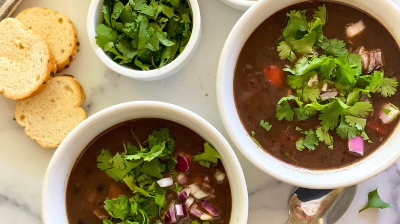 Bowls of black bean soup with sides of cilantro and crostini