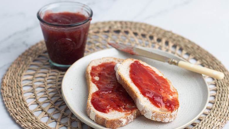 instant pot homemade strawberry jam in a glass jar and spread on two slices of toast on a white plate