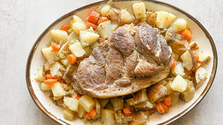 plate of pork surrounded by carrots and potatoes