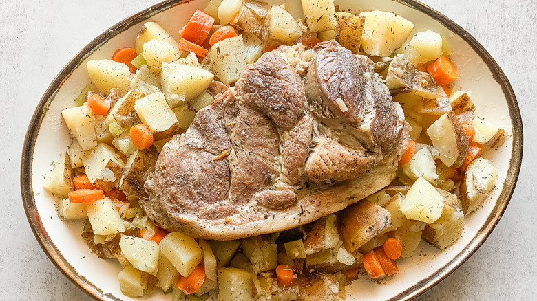 plate of pork surrounded by carrots and potatoes