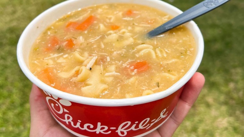 Hand holding Chick-fil-A chicken noodle soup in a branded red bowl