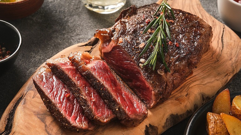 Sliced steak with herbs and seasoning on a cutting board