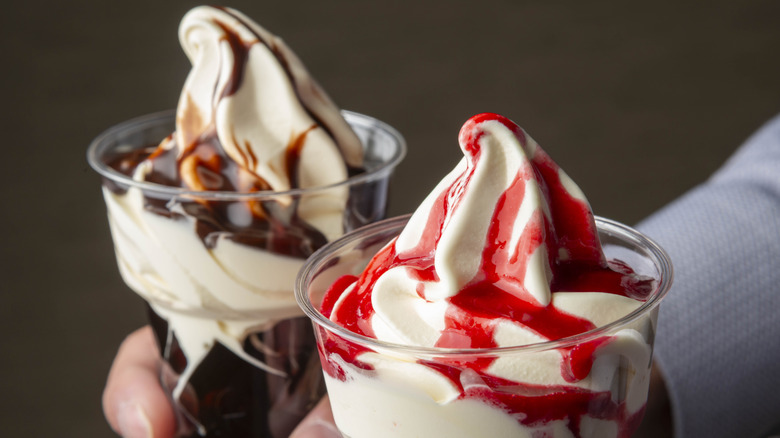 Two cups of soft serve with chocolate and strawberry drizzles