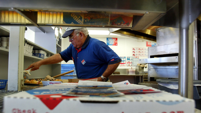 a Domino's pizza ready for pickup in store kitchen, an employee cuts a pizza in background