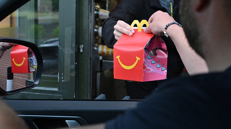 Fast food worker hands a Happy Meal box through drive thru window to man in car