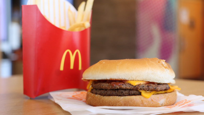 McDonald's double cheeseburger and carton of fries on table with restaurant blurred in background