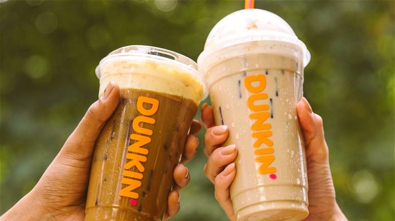 Two hands cheers with Dunkin' iced coffees