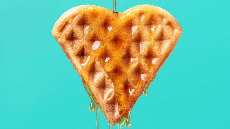 heart shaped waffle being covered in maple syrup