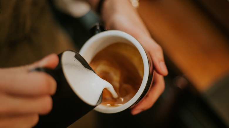 Person pouring milk into a latte 