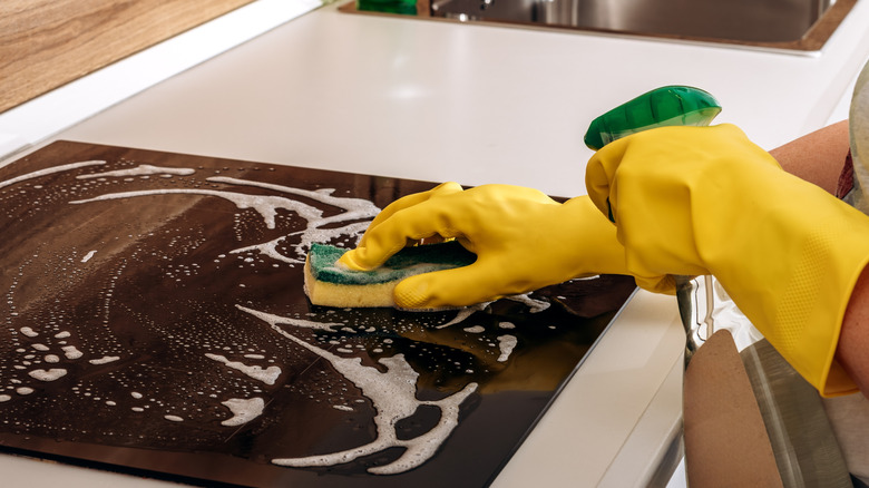Ceramic stovetop being cleaned with spray and a sponge.