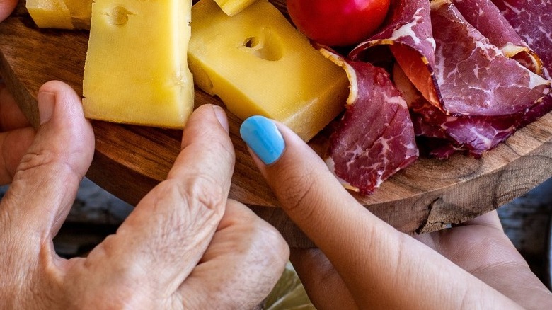 Close-up of hands reaching for cheeses and meats