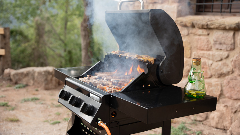 An open smoking grill with assorted meat and a pitcher of oil next to it