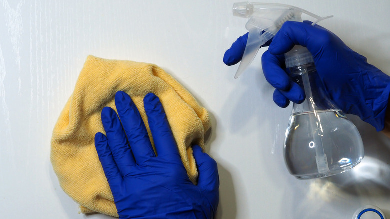Closeup of hands wearing blue cleaning gloves, holding a rag and cleaning spray bottle