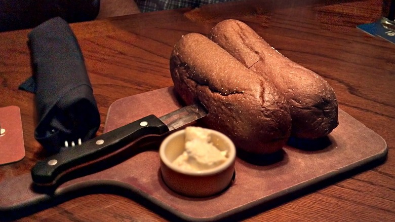 Two loaves of Outback Steakhouse bread secured with a knife, on a cutting board with a ramekin of butter