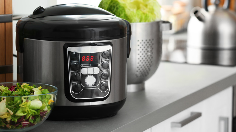 A slow cooker on a counter with a bowl of salad on the side