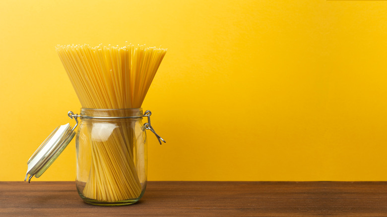 Jar of uncooked spaghetti against yellow backdrop