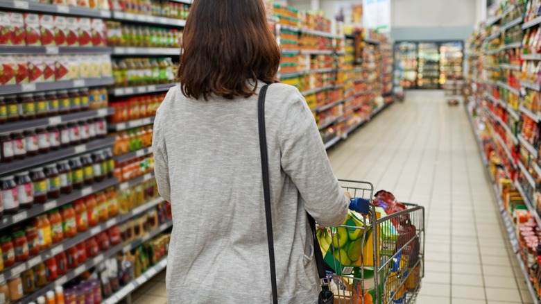 Person pushing a cart in a grocery store aisle