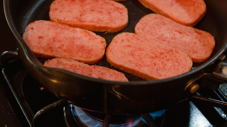 Slices of Spam frying in pan on stovetop.