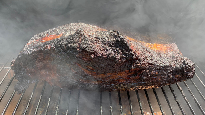 A large brisket smoking over a grill grate with perfect dark brown and black bark on the exterior.