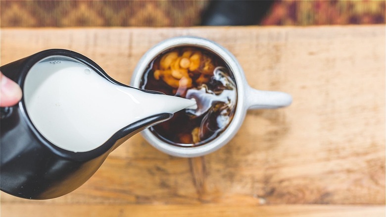 pouring milk into a cup of coffee on a wooden table