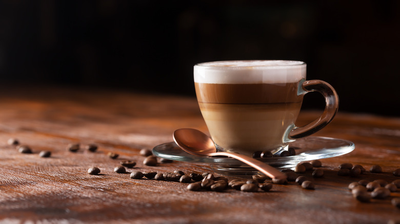 cup of coffee with milk and foam, coffee beans scattered around it, on a saucer with a spoon