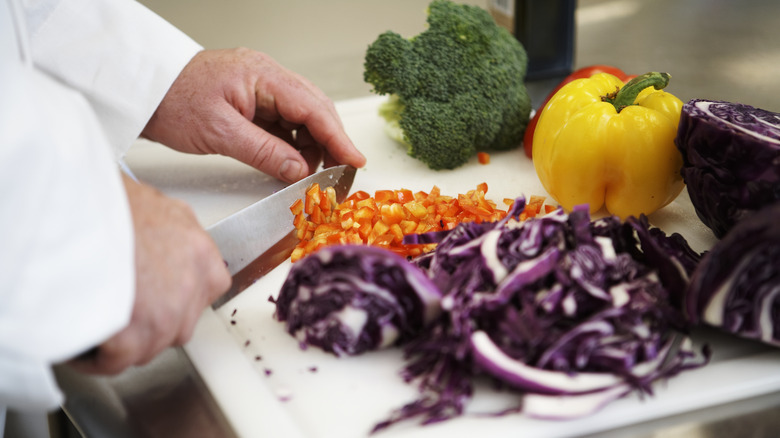 Hands chopping red peppers with a chef's knife 