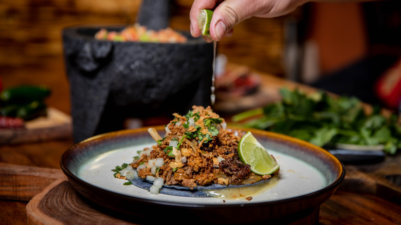 Hand squeezing lime juice onto a plated taco.