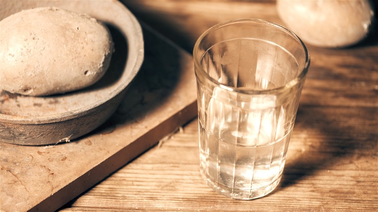 A glass of vodka next to a raw potato on a clay dish.
