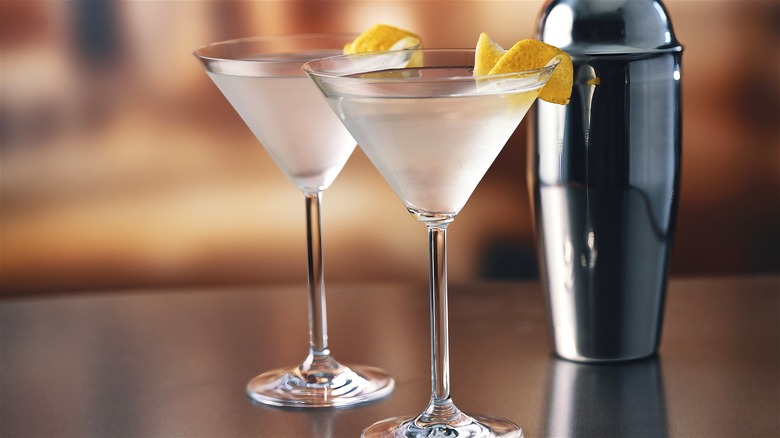 Two cold vodka martinis on a bar next to a shaker.