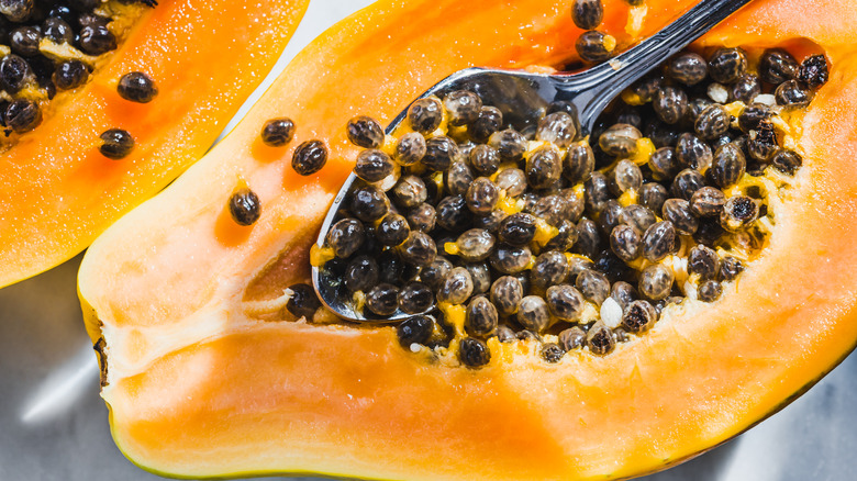 Papaya seeds being scooped out of papaya with silver spoon