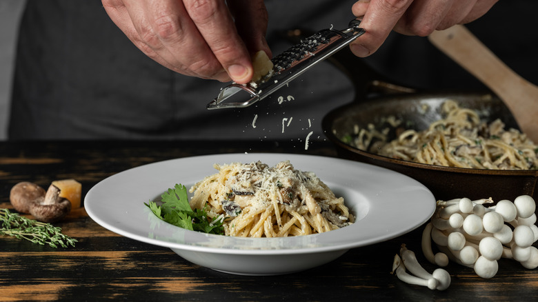 italian chef sprinkling cheese on pasta