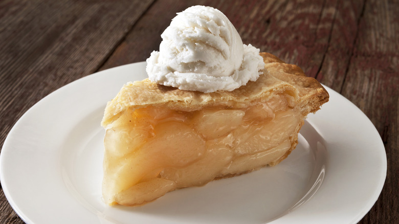 Slice of apple pie on a white plate topped with a scoop of vanilla ice cream