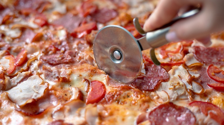 hand cutting a meat pizza