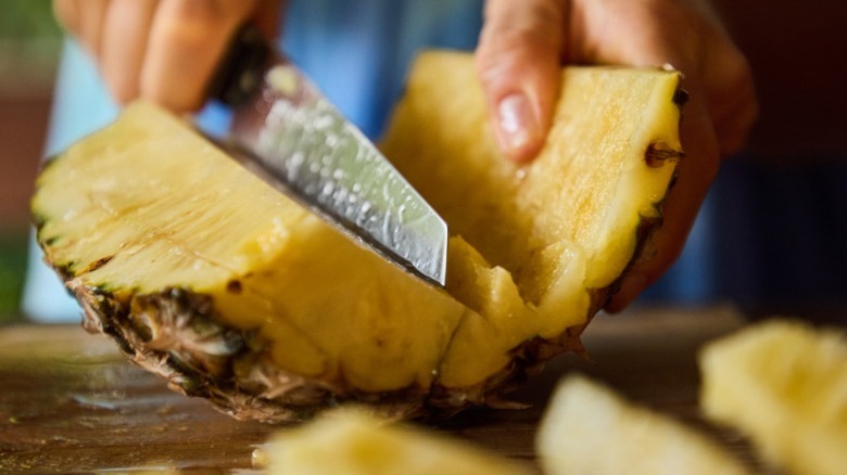 A person slicing half a whole pineapple