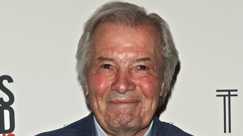 Jacques Pépin smiling in front of a white background.