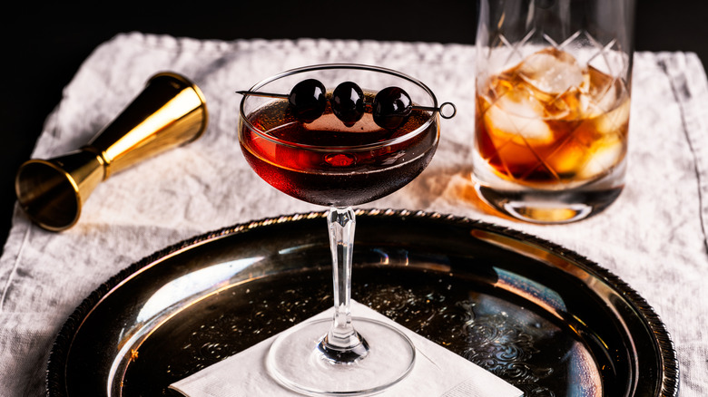 A Manhattan cocktail in a coupe glass with cherries, on a silver platter