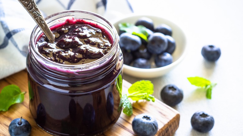 blueberry jam in a glass jar surrounded by fresh blueberries