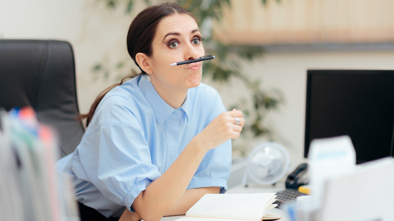 Woman avoiding work with pencil balanced on upper lip