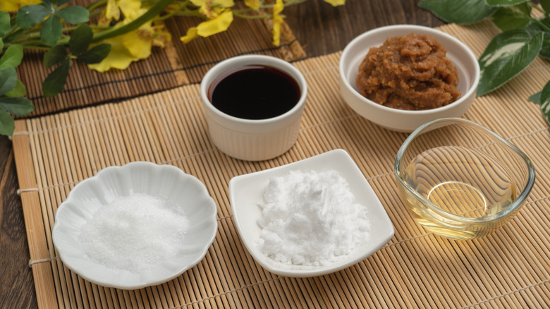 Sugar, salt, vinegar, soy sauce, and miso paste in containers on bamboo mat.