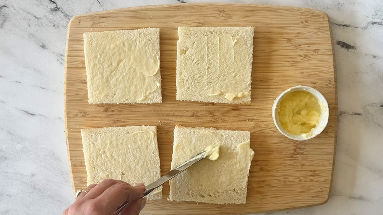 Knife spreading butter onto bread slices laid out on wooden board